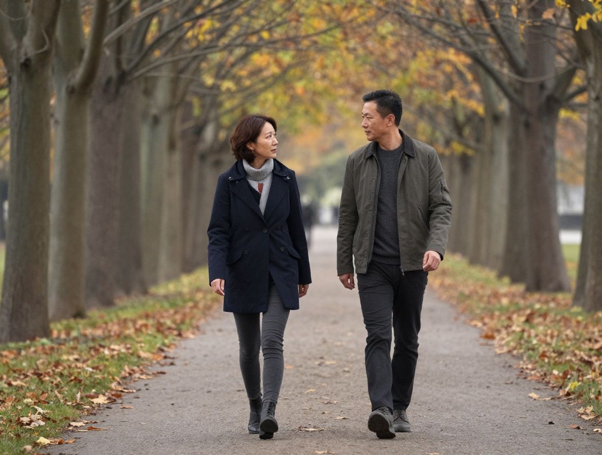 Two people walking together on a quiet tree-lined path in autumn, engaged in calm conversation, relaxed and natural outdoor setting